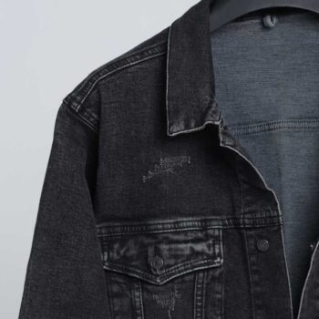 alt=“نمای نزدیک از پارچه جین زغالی و دکمه فلزی براق جکت DO57با کیفیت دوخت صنعتی و بافت سنگشوی طبیعی.”