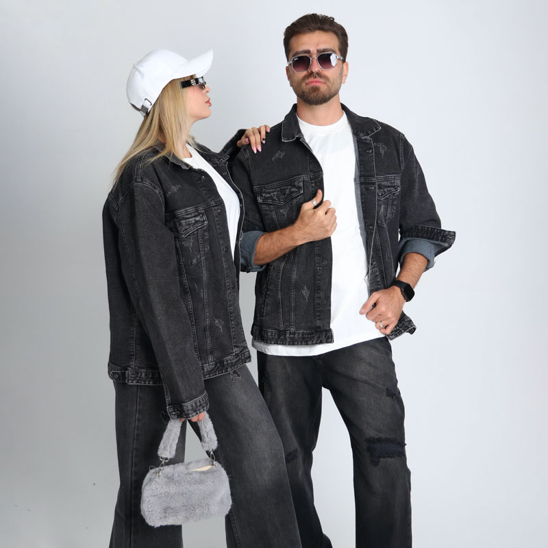 alt=“ست زوجی با جکت جین زغالی ساده DO57، استایل یونیسکس زغالی با تیشرت سفید و کفش اسپرت، پسزمینه شهری مدرن.”